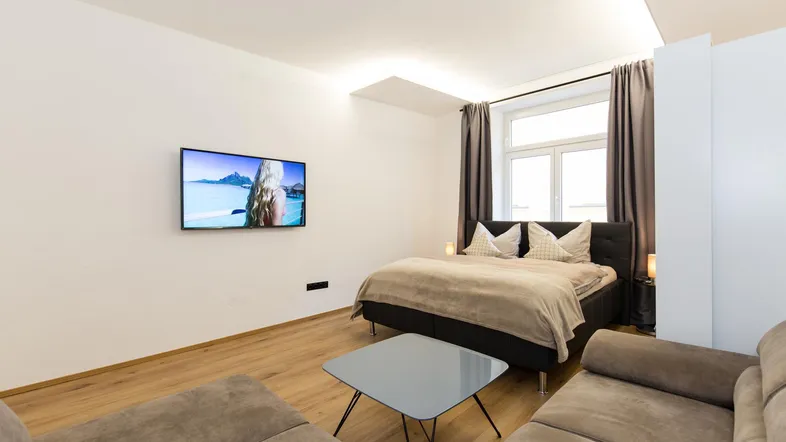 Modernes Schlafzimmer mit Holzboden, großem Bett und einem Flachbildfernseher an der Wand.