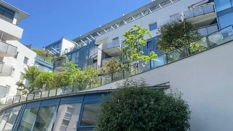 Moderne Wohnanlage mit gestuften Terrassen, Glasfassaden und üppiger Bepflanzung unter blauem Himmel.