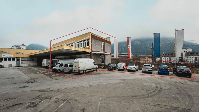 Außenansicht eines Gewerbegebäudes mit großem Parkplatz und Lieferwagen, umgeben von Bergen.