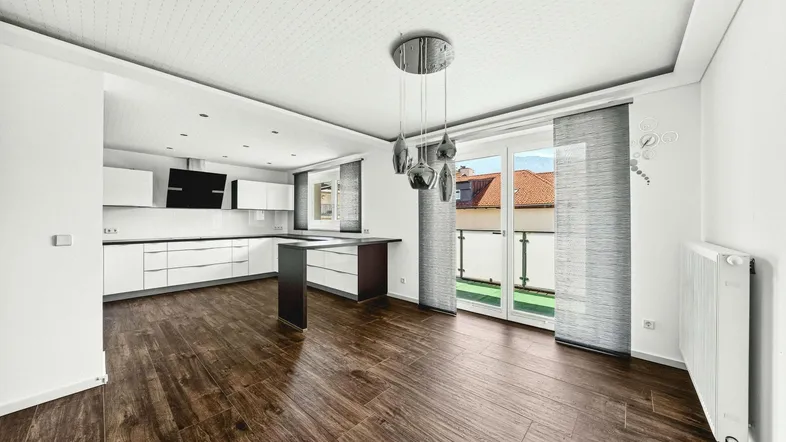 Heller offener Wohn- und Essbereich mit moderner Einbauküche, dunklem Holzboden und Zugang zum Balkon.