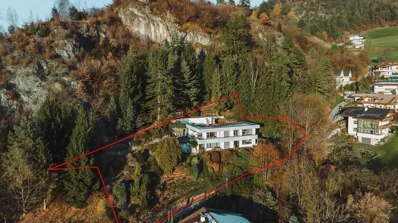 Luftaufnahme des modernen Hauses auf einem bewaldeten Hügel mit markierter Grundstücksgrenze und Bergblick.