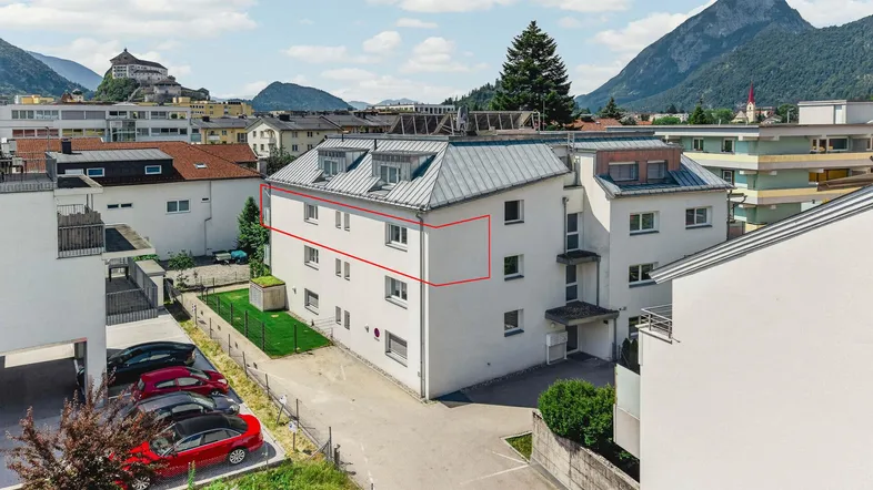 Gebäudeansicht von oben mit umliegender Bebauung und Bergkulisse im Hintergrund.