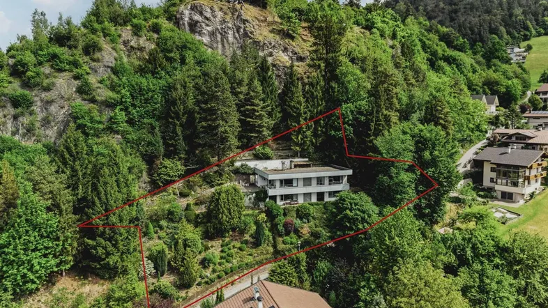 Luftaufnahme eines Hauses am Hang mit viel Grün und umrandetem Grundstück.