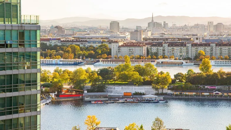 Panoramablick auf die Stadt mit Fluss, modernen Gebäuden und Bergen im Hintergrund.