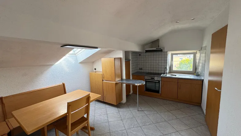 Küche mit Essbereich, Holzmöbeln, Fliesenboden und einem Dachfenster für natürliches Licht.