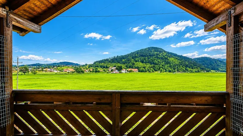Überdachter Balkon mit Holzbalken und weitem Blick auf grüne Felder und Berge.