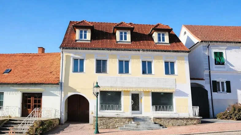 Traditionelles Gebäude mit gelber Fassade, rotem Ziegeldach und mehreren Dachgauben in ländlicher Umgebung.