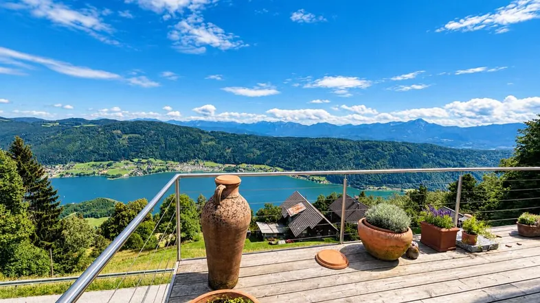 Große Holzterrasse mit atemberaubendem Blick auf den See und die umliegenden Berge unter blauem Himmel.