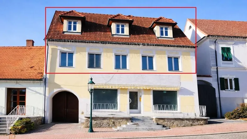 Historisches Gebäude mit gelber Fassade, rotem Ziegeldach und Gaubenfenstern an einer gepflasterten Straße.