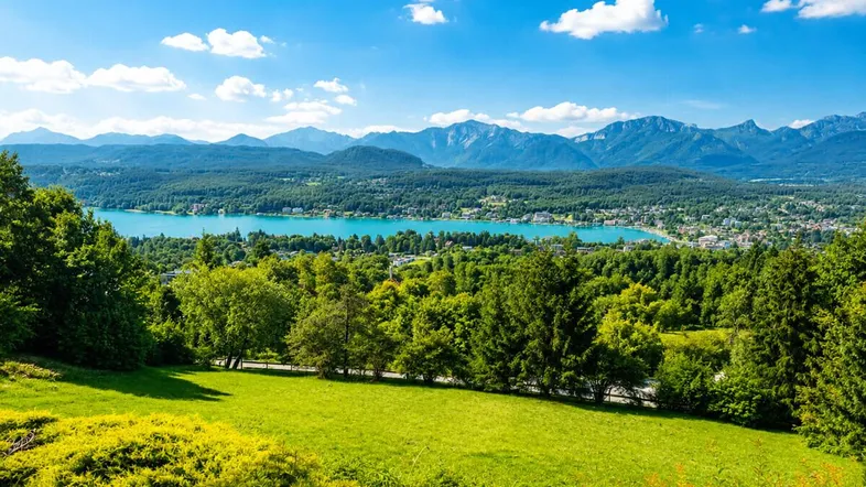 Panoramablick auf einen See mit Bergen und üppiger grüner Landschaft unter blauem Himmel.
