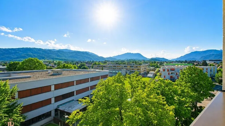Sonniger Ausblick auf die umliegende Berglandschaft und grüne Umgebung von einem Balkon.