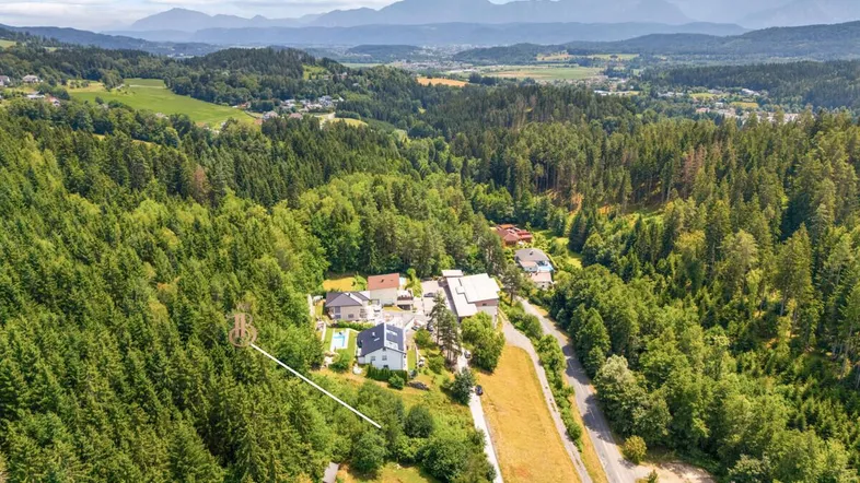 Panoramablick auf das Grundstück, eingebettet in eine grüne Landschaft mit Bergen am Horizont.
