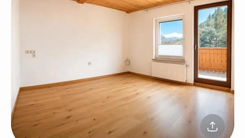 Helles Zimmer mit Holzbalkendecke, Parkettboden und Zugang zu einem Balkon mit Bergblick.