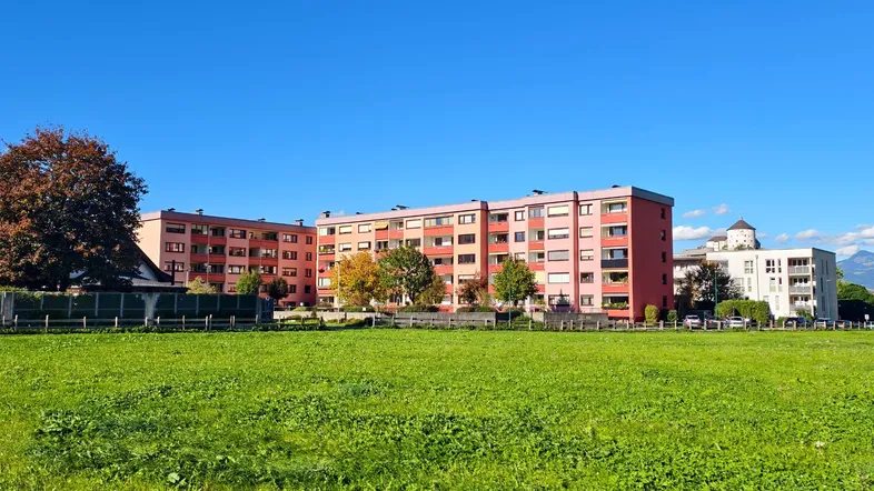 Mehrere Wohngebäude mit roter Fassade und weitem Grünflächenblick unter blauem Himmel.