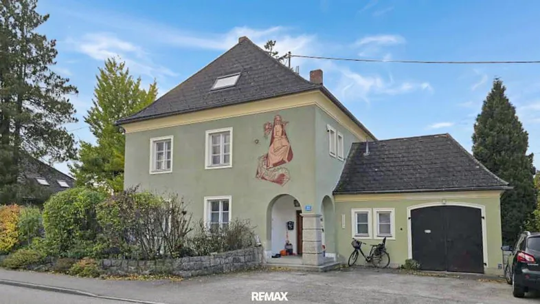 Historisches Haus mit grünlicher Fassade, Wandgemälde und integrierter Garage.