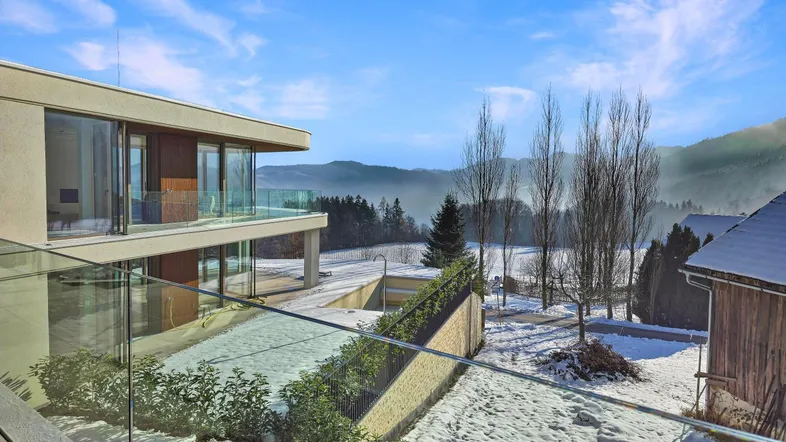 Modernes Gebäude mit Glasbalkonen und weitem Blick auf die verschneite Landschaft und Berge.