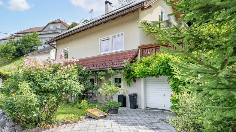 Einfamilienhaus mit gepflasterter Einfahrt, Garage und blühenden Rosenbüschen im Vorgarten.