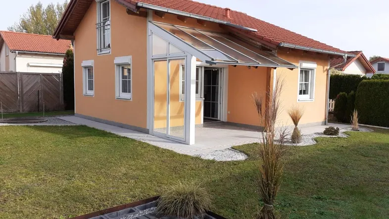 Modernes Einfamilienhaus mit orangefarbener Fassade, Wintergarten und gepflegtem Gartenbereich.