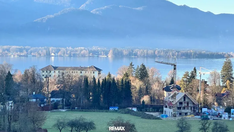 Weitläufiger Blick auf den See mit umliegenden Bergen und Häusern am Ufer.