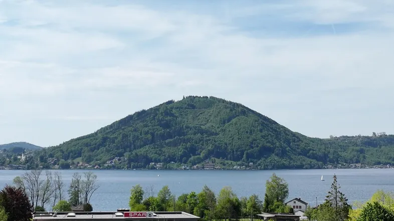 Panoramablick auf den See und die umliegenden Berge mit einem Supermarkt im Vordergrund.