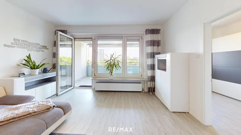 Helles Wohnzimmer mit hellem Laminatboden, modernen Möbeln und Zugang zu einem Balkon mit Grünblick.