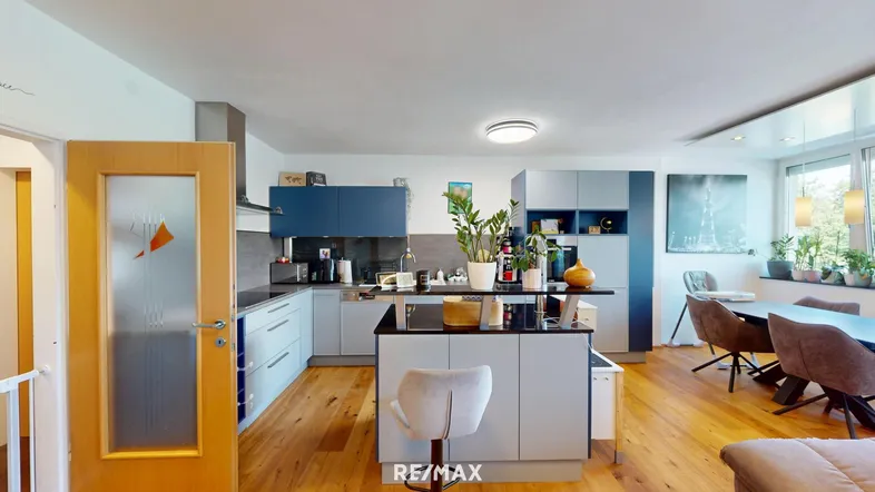 Moderne offene Küche mit blaugrauen Schränken, Kücheninsel und Essbereich im Hintergrund.