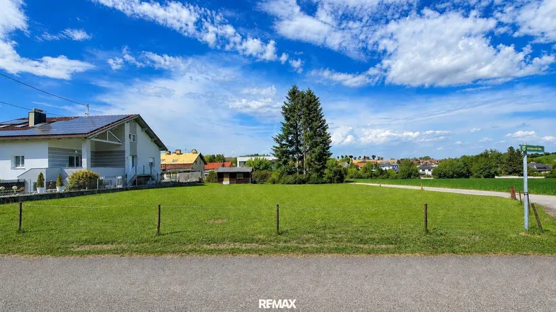 Weitläufige grüne Wiese mit einem Einfamilienhaus im Hintergrund unter blauem Himmel.