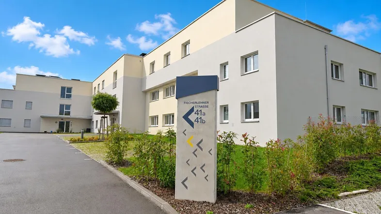 Modernes Mehrfamilienhaus mit heller Fassade und Wegweiser zur Adresse.
