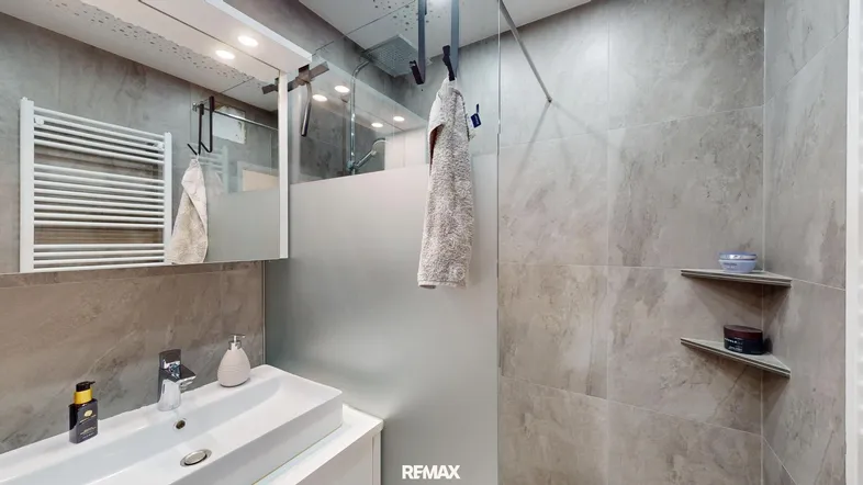 Modernes Badezimmer mit grauen Fliesen, begehbarer Dusche, Waschbecken und beheiztem Handtuchhalter.