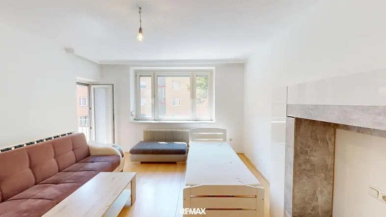 Helles Wohnzimmer mit Sofa, Bett und großem Fenster, das viel Tageslicht hereinlässt.