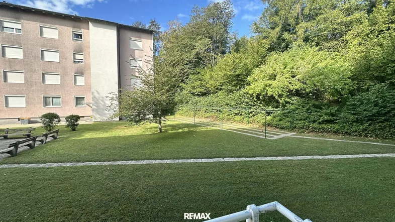 Gepflegte Grünfläche mit Sitzbänken vor dem Mehrfamilienhaus, umgeben von Bäumen und Sträuchern.