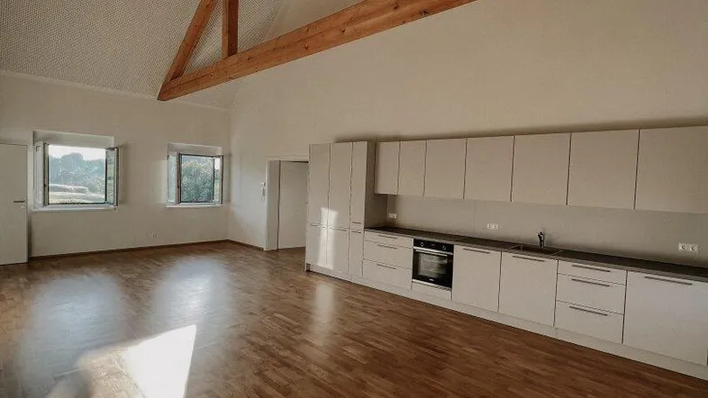 Heller offener Wohnbereich mit moderner Einbauküche, Holzbalken und Parkettboden.
