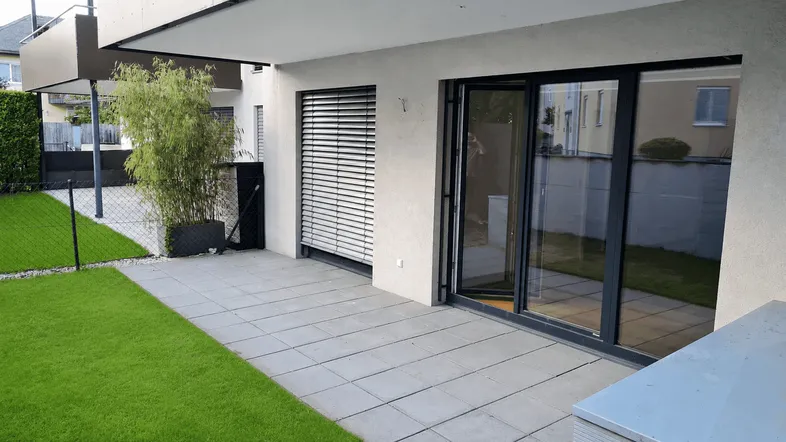 Große gepflasterte Terrasse mit angrenzendem Rasen und Zugang zu den Innenräumen.