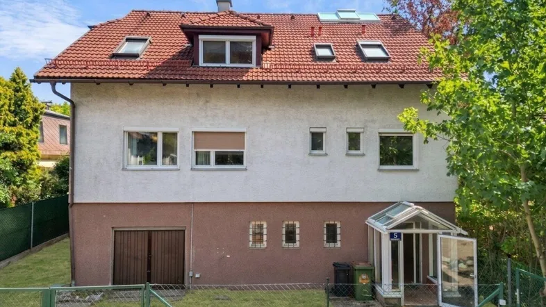 Älteres Einfamilienhaus von der Rückseite mit Gartenbereich und Garagenzugang.