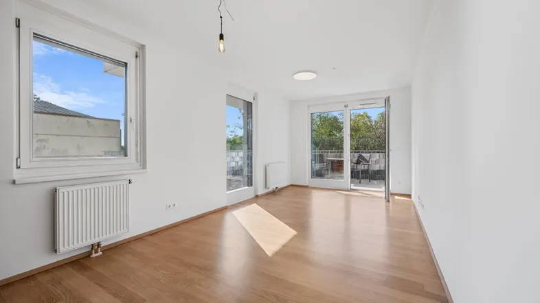 Helles, leeres Wohnzimmer mit Parkettboden und Zugang zu einem Balkon, ideal für individuelle Gestaltung.