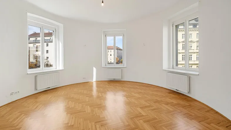 Helles Zimmer mit einzigartiger runder Wand und Fischgrätparkettboden, ideal für einen Wohnbereich.