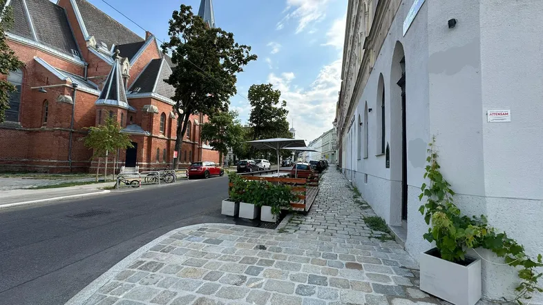 Blick auf eine belebte Straße mit einer Kirche, einem Gebäude und einer Außenterrasse mit Sitzgelegenheiten.