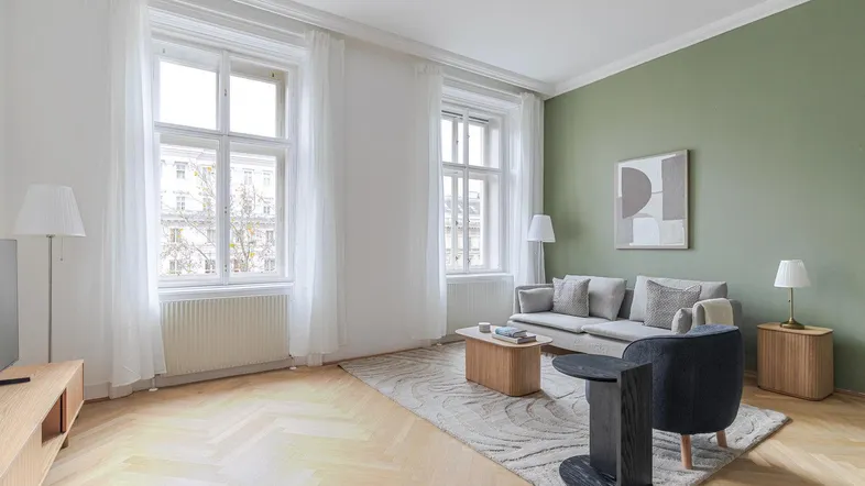 Helles Wohnzimmer mit Fischgrätparkett, grüner Akzentwand und modernen Möbeln.