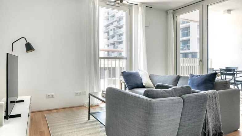 Helles Wohnzimmer mit modernem Sofa, Holzboden und Zugang zum Balkon mit Stadtblick.