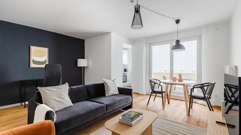 Helles Wohn- und Esszimmer mit Holzboden, modernem Sofa und Zugang zum Balkon.