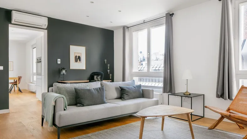 Modernes Wohnzimmer mit grauem Sofa, Holzboden, dunkler Akzentwand und Klimaanlage.