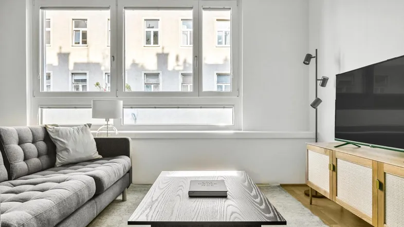 Helles Wohnzimmer mit modernem Sofa, Couchtisch und großen Fenstern mit Blick auf die Stadt.