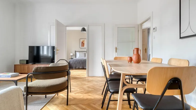 Heller Wohn- und Essbereich mit Fischgrätparkett und Zugang zu einem weiteren Zimmer.