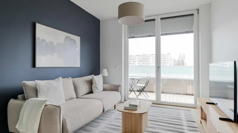 Modernes Wohnzimmer mit beigem Sofa, dunkler Akzentwand und Zugang zum Balkon.