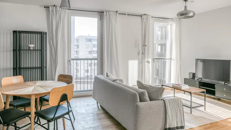 Helles Wohn- und Esszimmer mit Holzboden, bequemer Couch und Zugang zum Balkon.