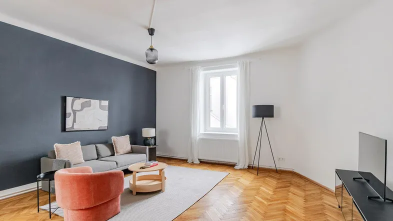 Geräumiges Wohnzimmer mit Fischgrätparkett, einer dunkelblauen Akzentwand und moderner Einrichtung.