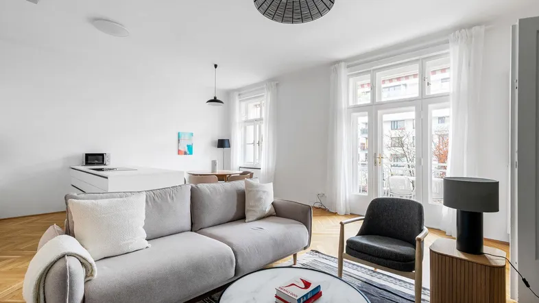 Helles Wohnzimmer mit modernem Sofa, Parkettboden und großen Fenstern, offen zum Essbereich.