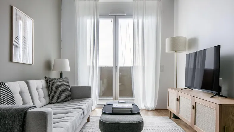 Helles Wohnzimmer mit modernem Sofa, Teppich und Zugang zu einem Balkon.