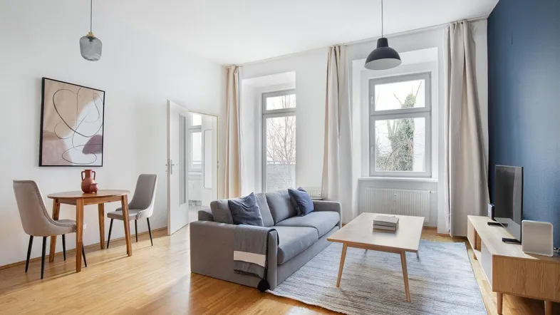 Helles Wohnzimmer mit Holzboden, grauem Sofa und integriertem Essbereich.