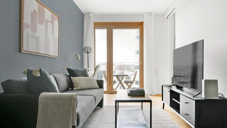 Helles Wohnzimmer mit modernem Sofa, Fernseher und Zugang zum Balkon mit Stadtblick.